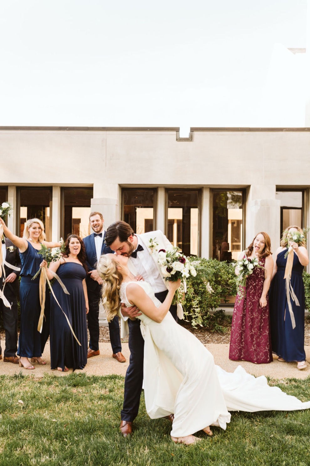 bride and groom kissing while bridal party looks on