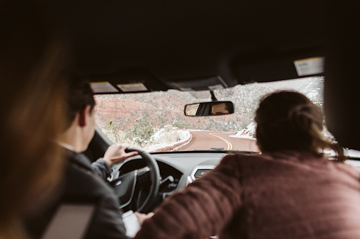 Bride and groom driving a curvy road toward red cliffs