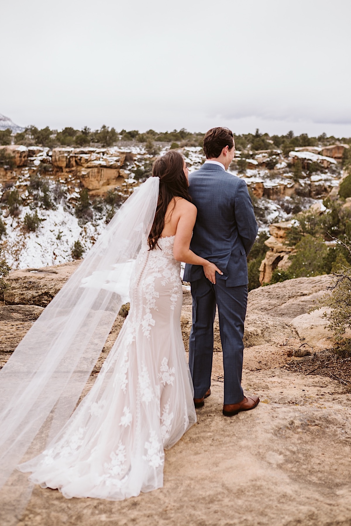 Bride wearing lacy strapless dress and long veil sneaks up on groom for first look and slaps his butt