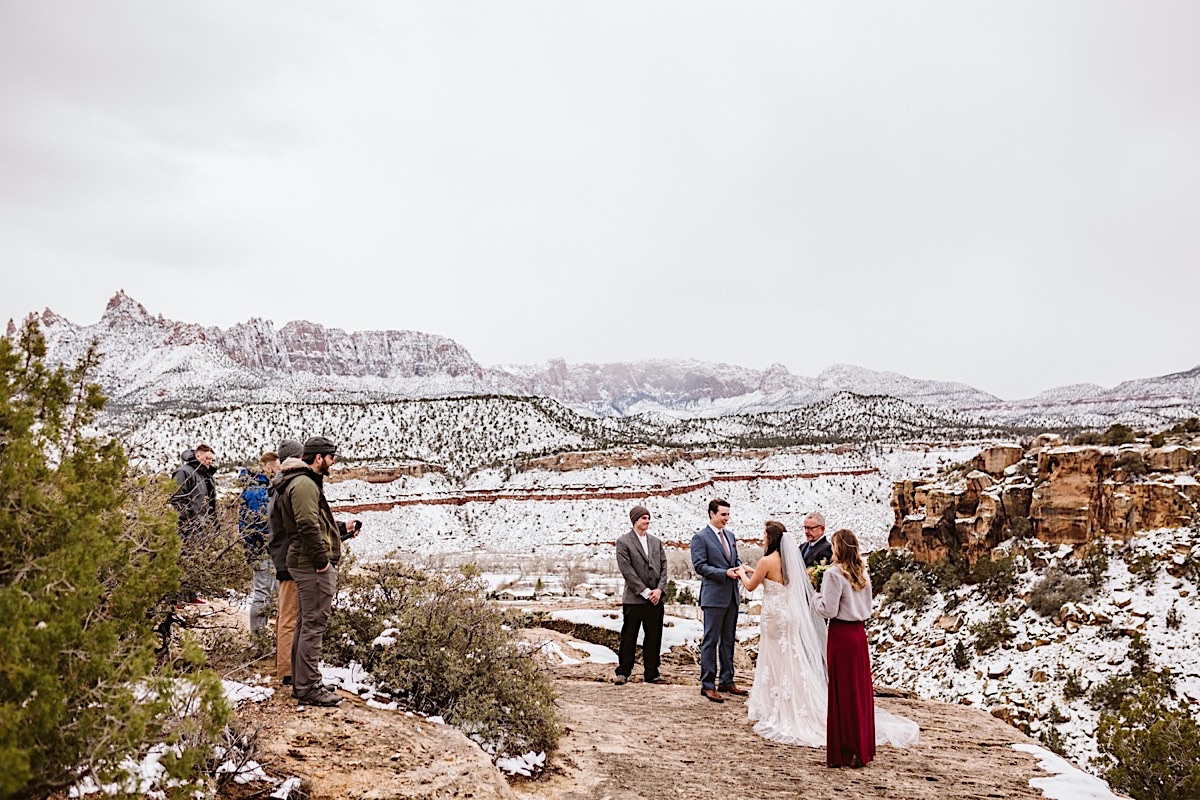 Bride and groom hold hands and exchange vows during their elopement ceremony on a cliff while a few friends watch