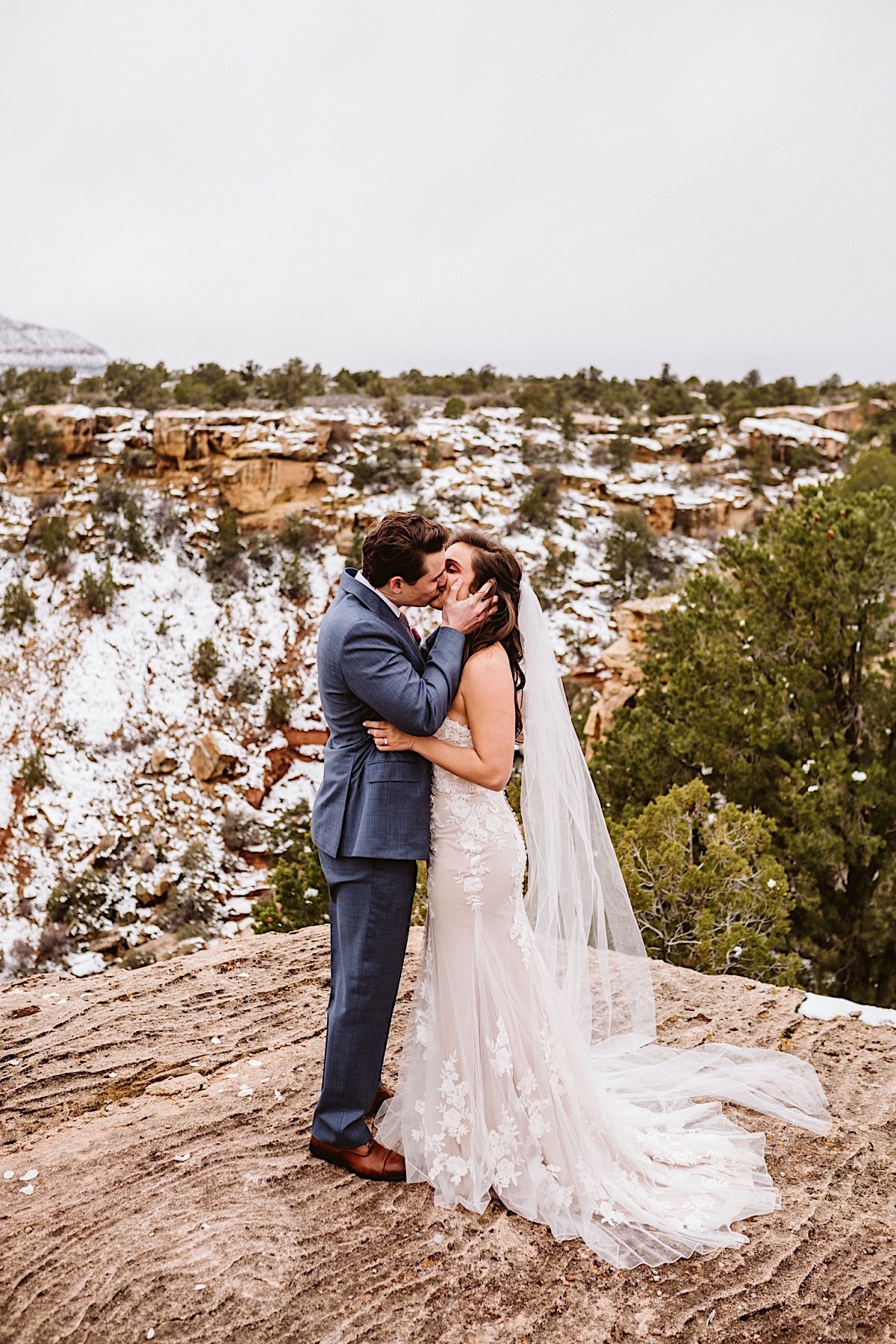 Bride and groom kiss on the edge of a cliff with a foggy snowy sky
