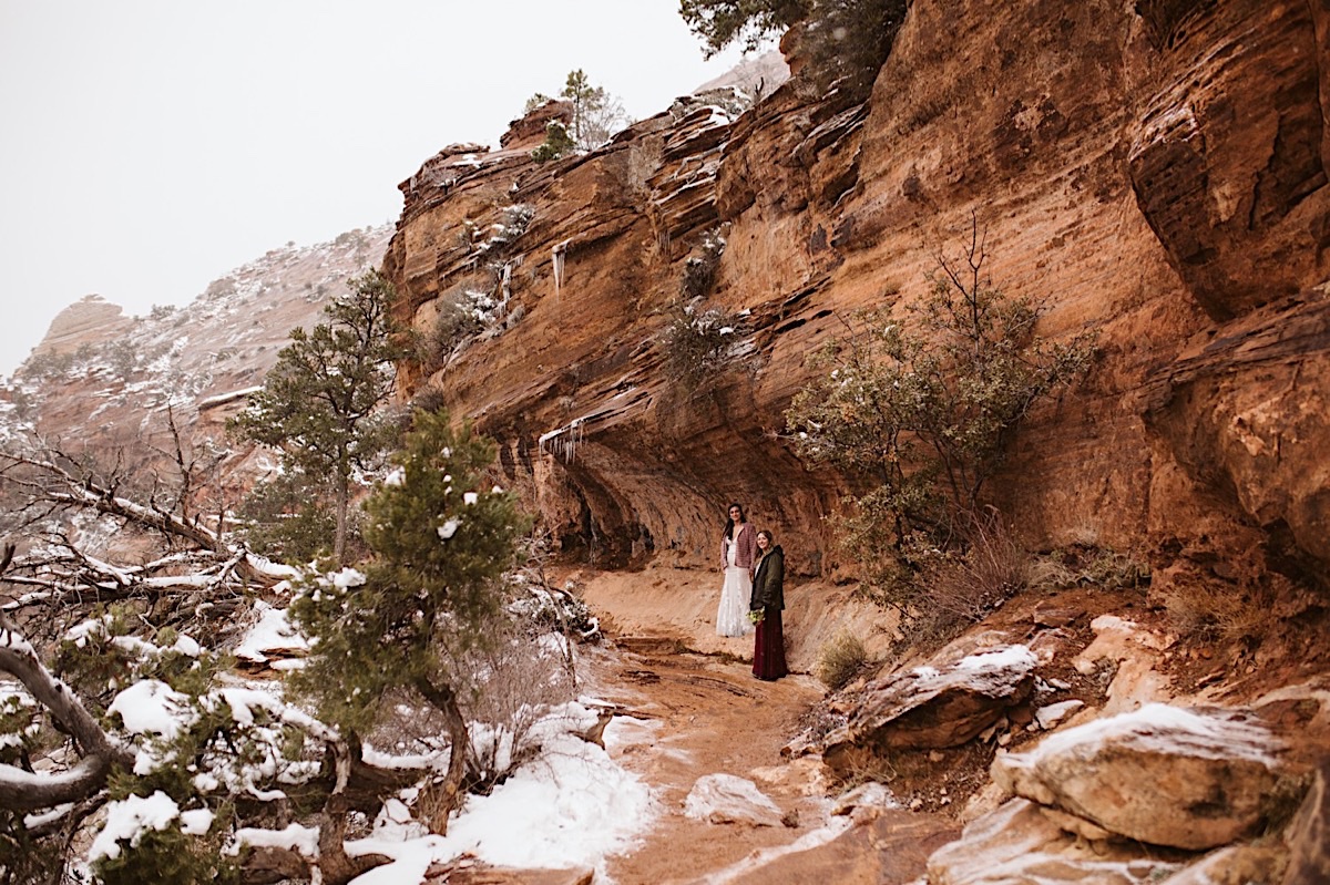 Bride and bridesmaid at the bottom of red cliffs hiking to Canyon Overlook
