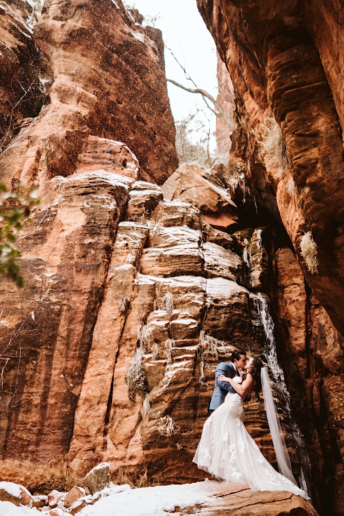 Bride and groom kiss at the bottom of red cliffs at Zion National Park.