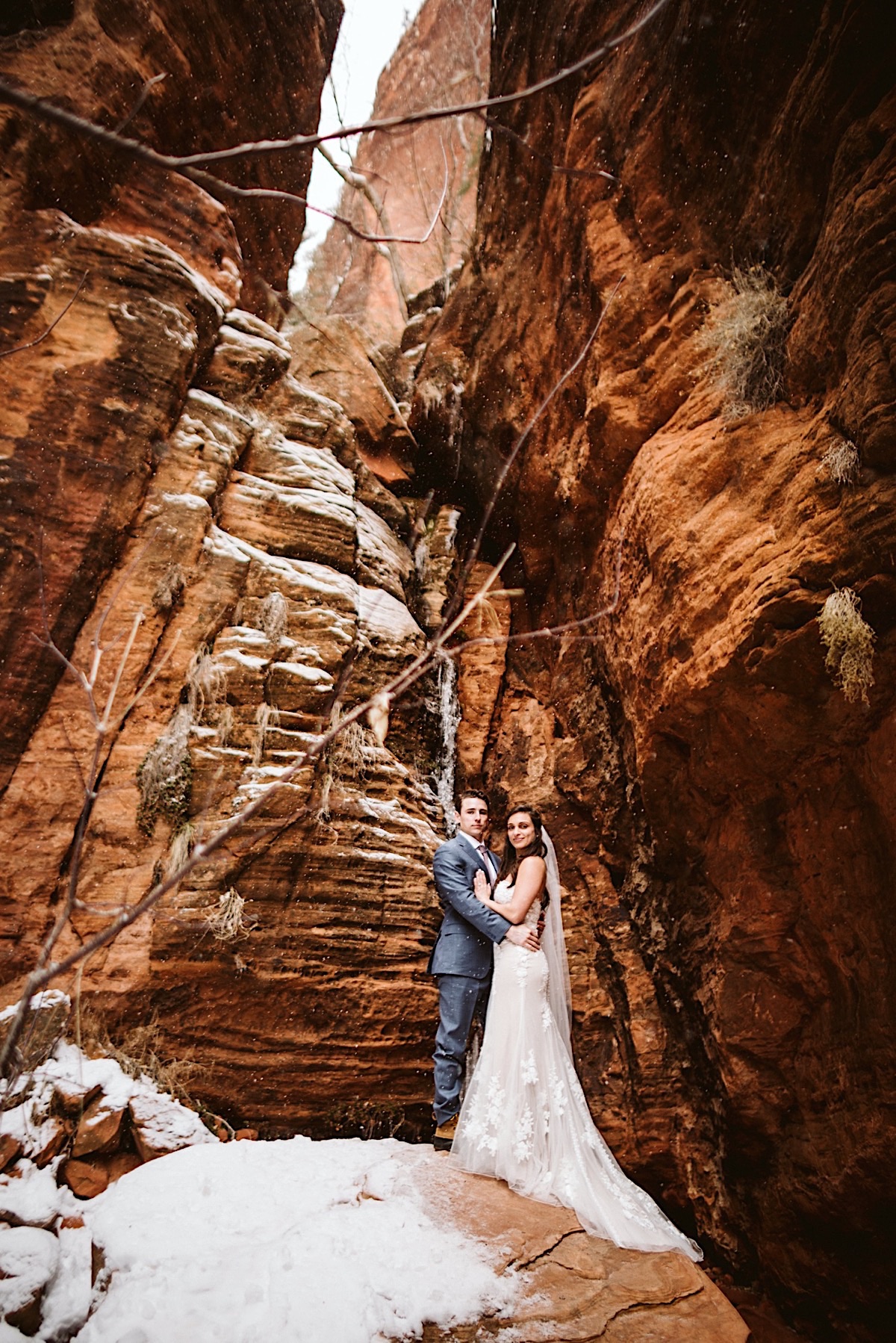 Bride and groom pose at the bottom of red cliffs at Zion National Park.