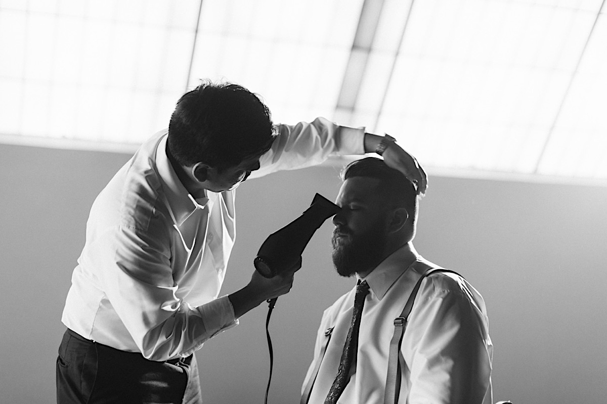 Man sits with eyes closed while a friend holds hair dryer and shapes his hair