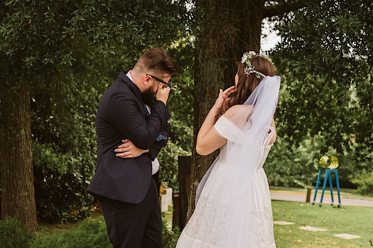 Bride covers her mouth as groom wipes his eyes during their tearful first look.