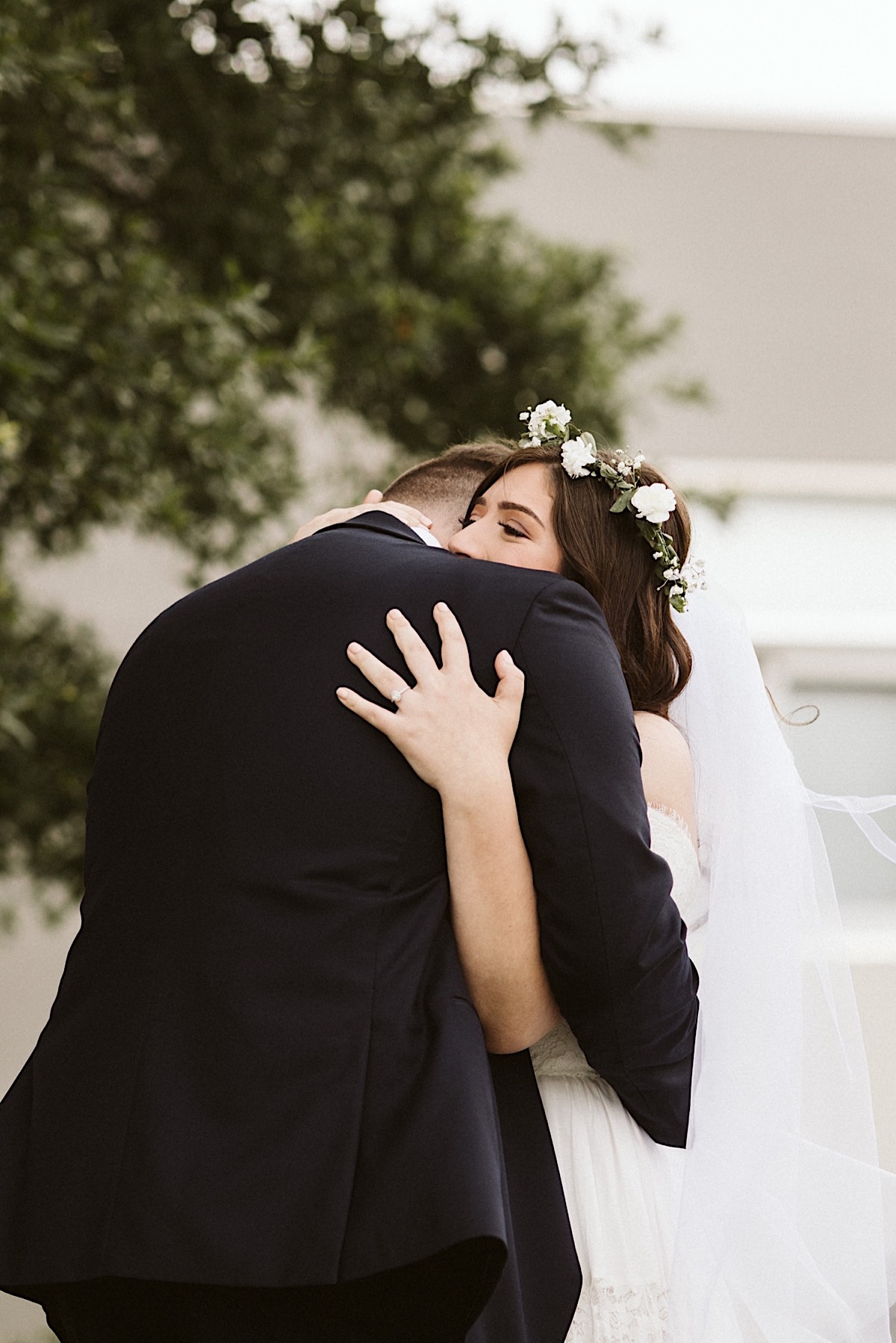 Bride and groom hug, her hand gripping the back of his shoulder.