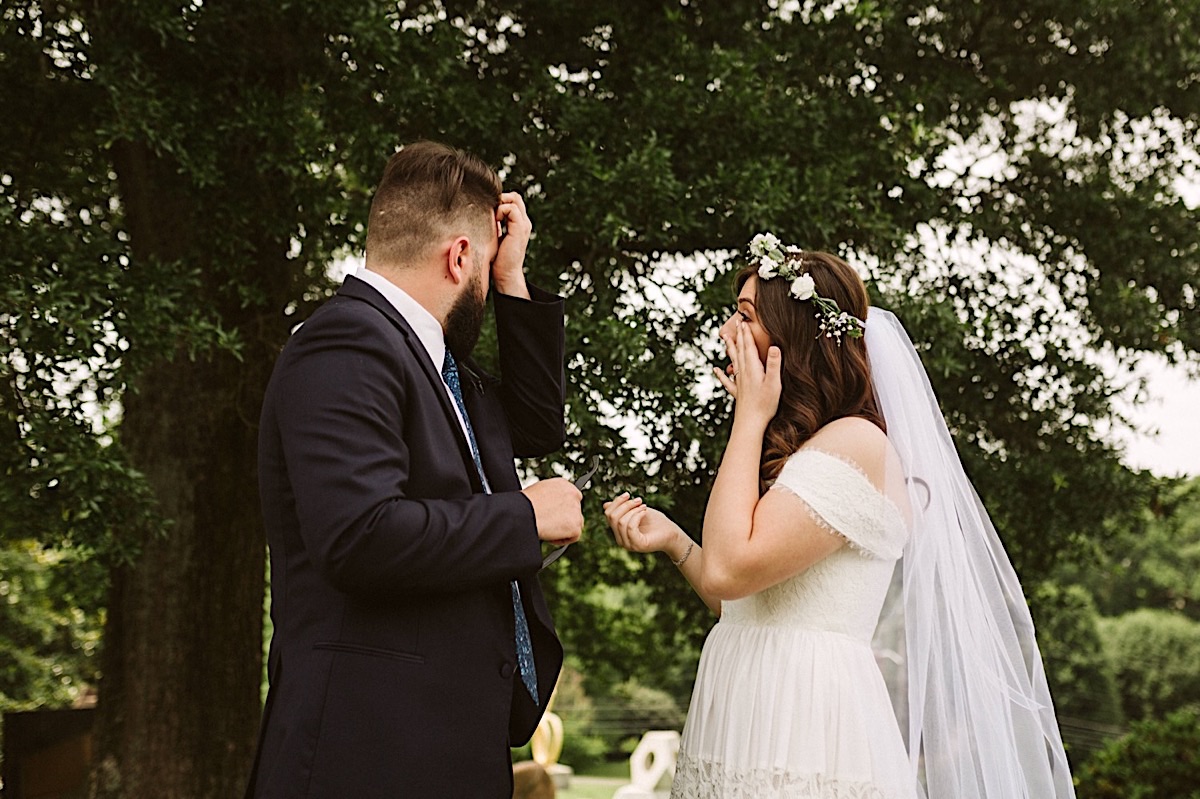 Bride and groom wipe their eyes after a tearful first look. She wears a veil tucked into her floral crown