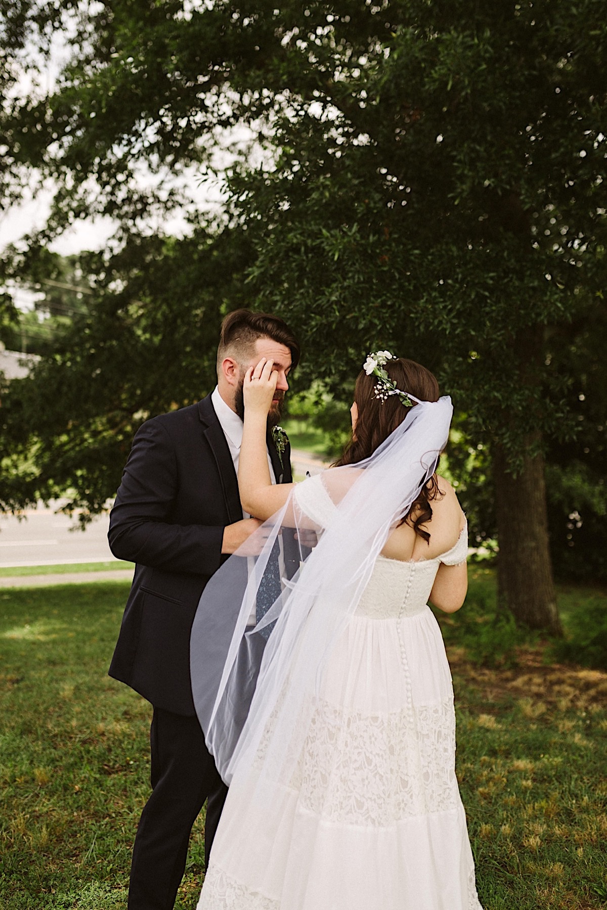 Bride clears grooms eyes, her veil blowing in a breeze