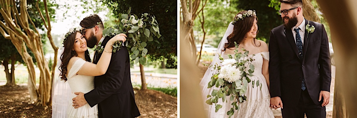 Bride and groom cuddle under crepe myrtles. She holds a large bouquet of white flowers and eucalyptus leaves.