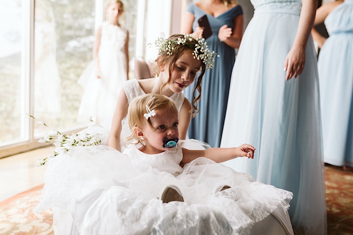 Flower girl wears a white flower crown and another has a white barrette in her hair