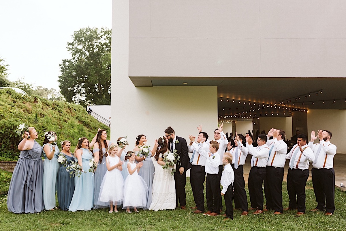 Bride and groom kiss, surrounded by their wedding party outside the Creative Arts Guild in Dalton, Georgia.