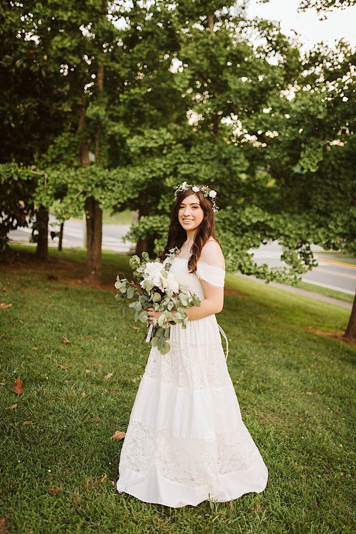 Bride wears a lacy white gown and white flower crown in her dark hair. She holds white floral bouquet and eucalyptus greens.
