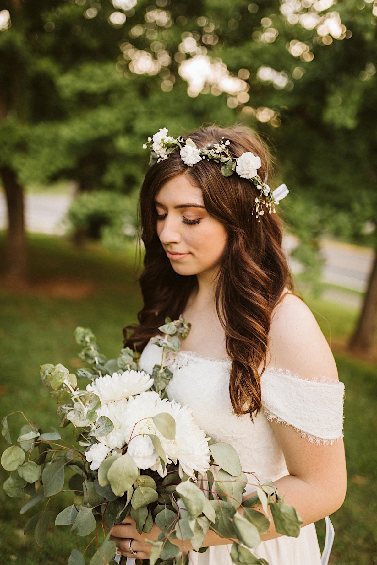 Bride wears a white flower crown in her dark hair. She looks down at her white floral bouquet with eucalyptus greens.