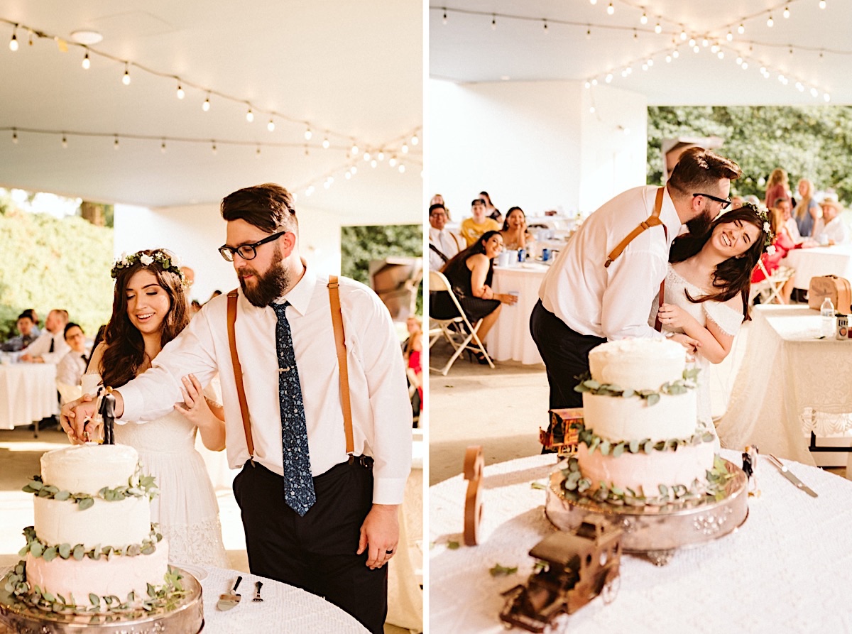 Bride and groom cut into their 3-tier white wedding cake, each layer offset by eucalyptus leaves.