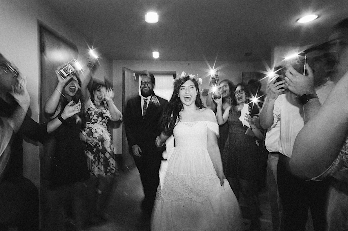 Bride and groom exit through a makeshift "sparkler" tunnel. Guests hold cellphones to light their way.