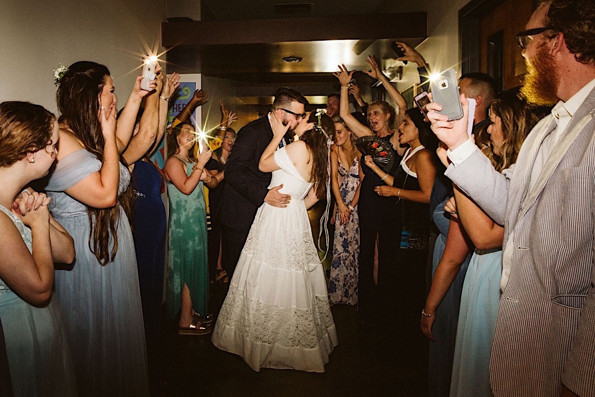 Bride and groom kiss under a makeshift "sparkler" tunnel. Guests hold cellphones to light their way.