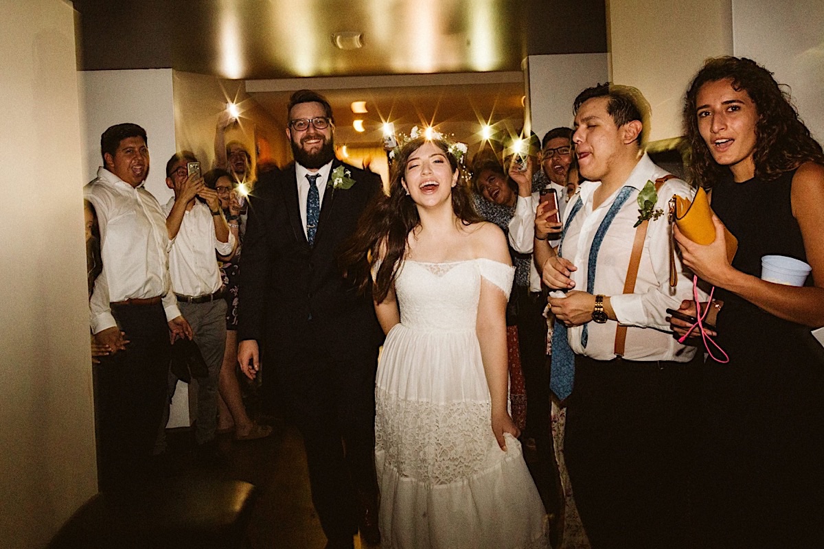 Bride and groom exit through a makeshift "sparkler" tunnel. Guests hold cellphones to light their way.