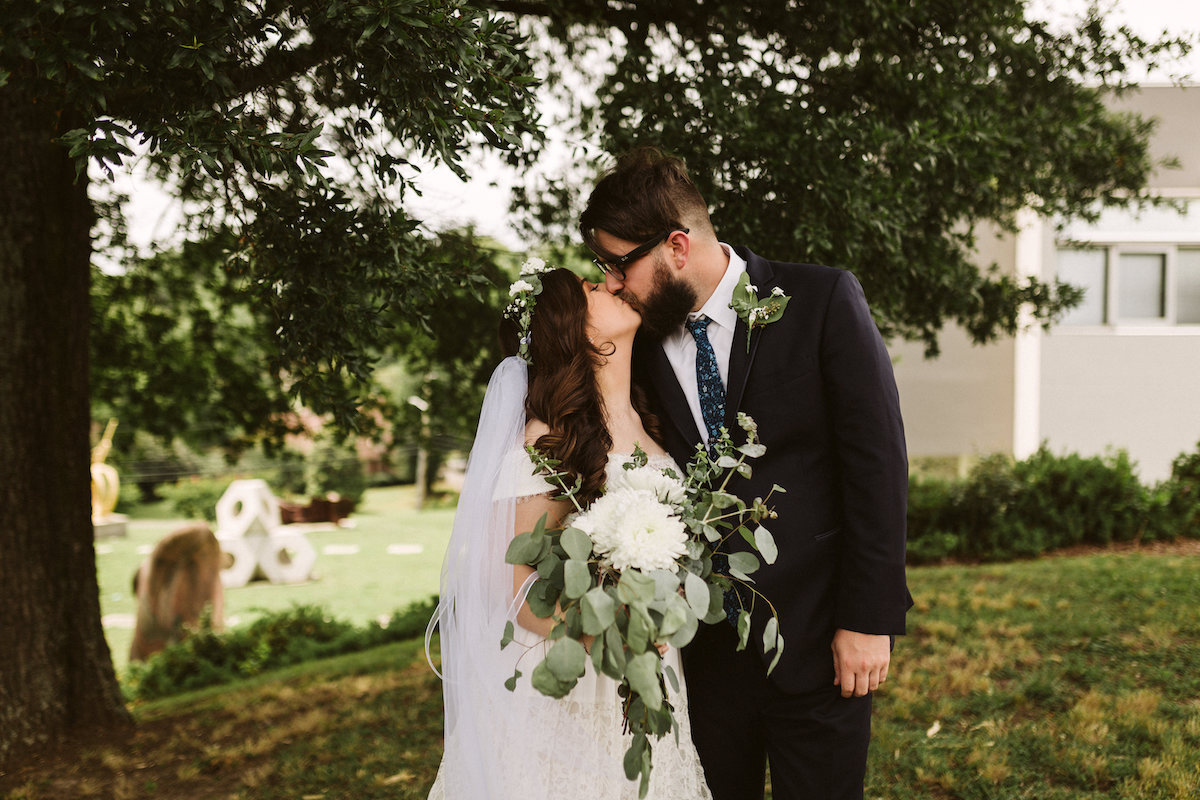 Bride and groom kiss in front of the Creative Arts Guild in Dalton, Georgia. Her white bouquet falls over his shoulder.