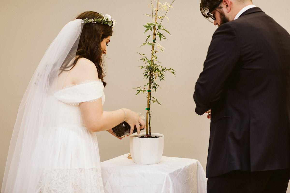 Bride and groom plant a tree together in a white pot their Creative Arts Guild wedding in Dalton, Georgia.