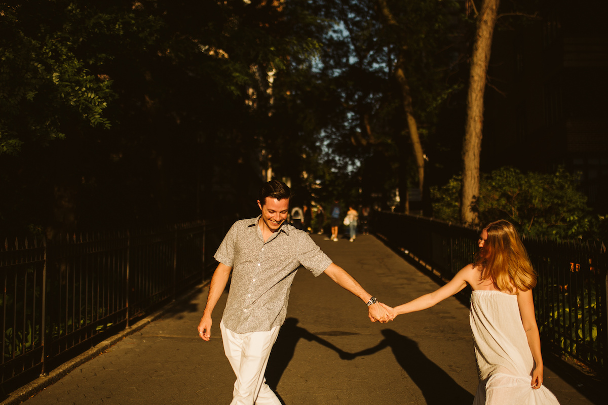 Man and woman hold hands and walk between black metal fencing.