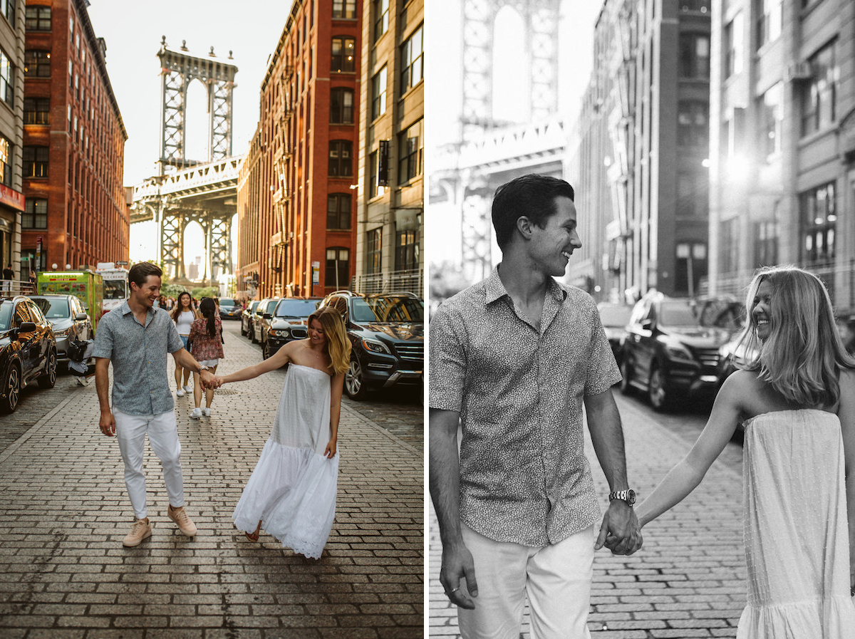 Man and woman hold hands, smiling at each other, while walking down brick street with Brooklyn Bridge in the background