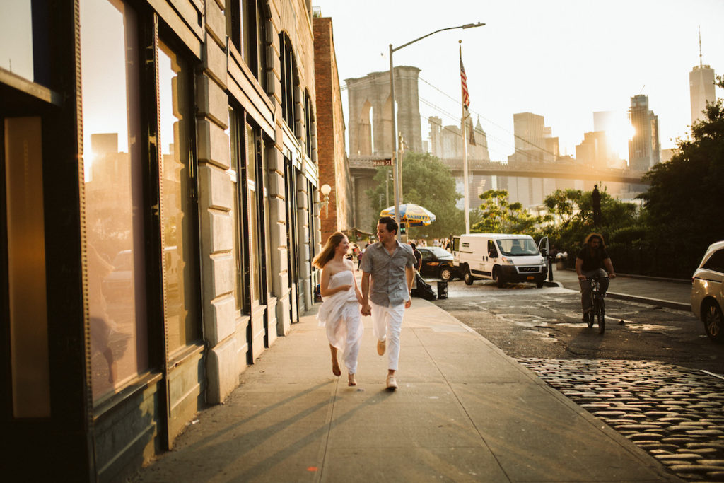 Man and woman run down the sidewalk next to cobblestone street near the Brooklyn Bridge