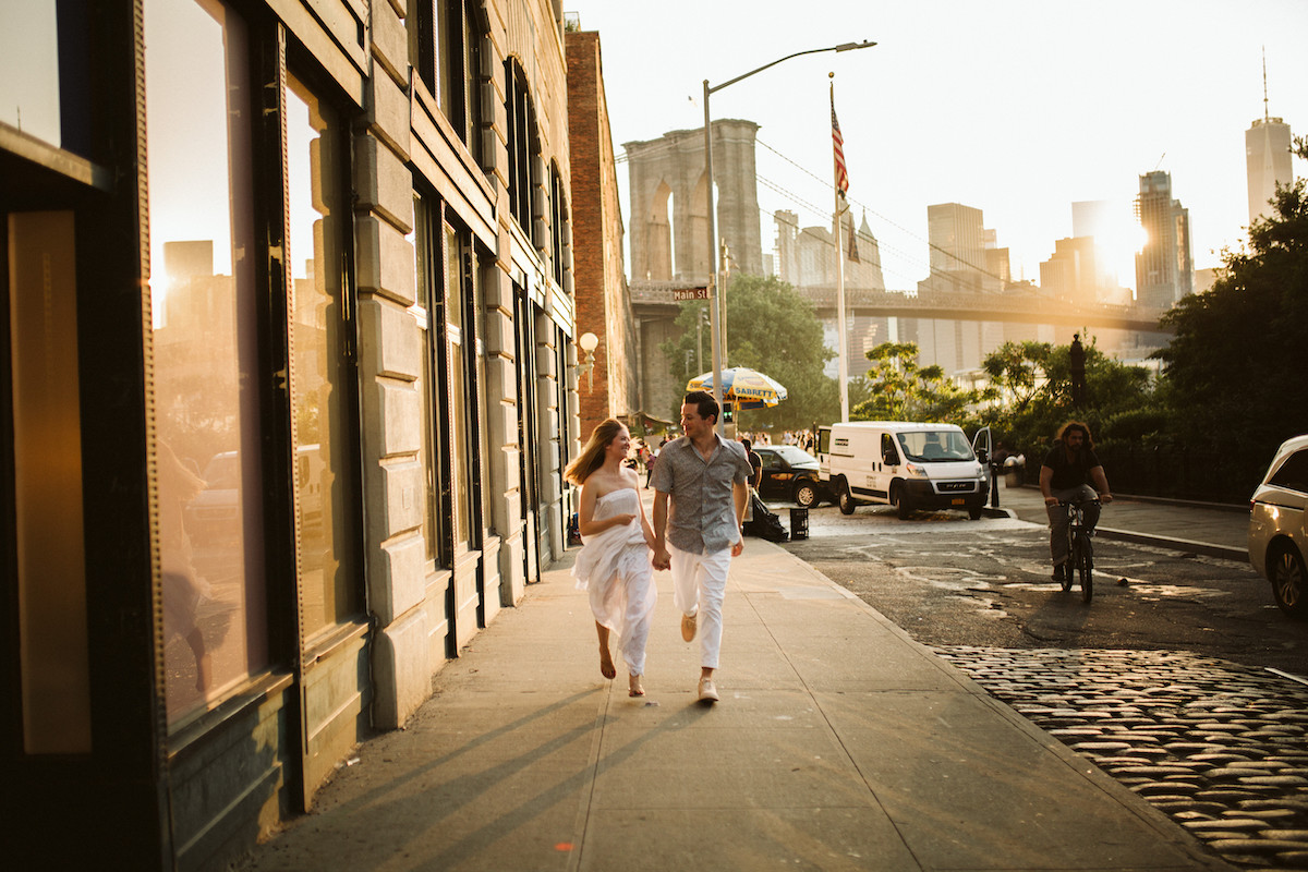 Man and woman run down the sidewalk next to cobblestone street near the Brooklyn Bridge