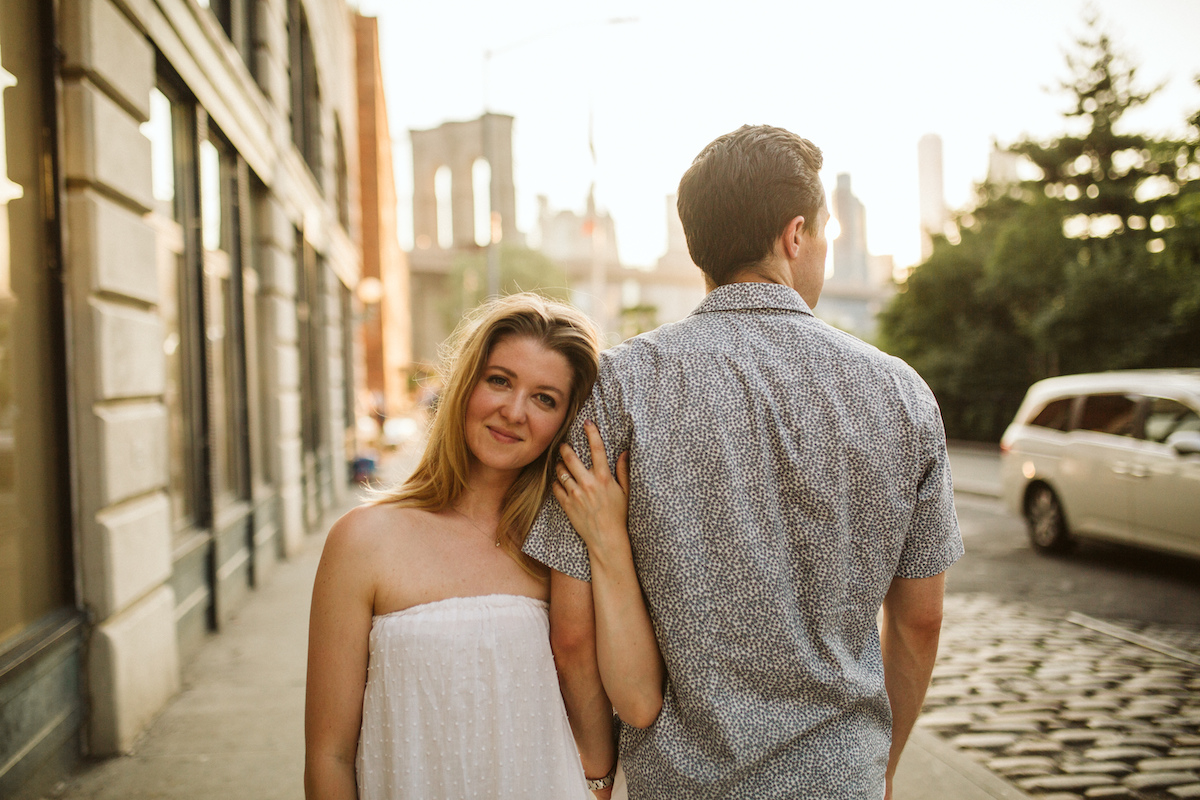 Man and woman hold each other on the sidewalk during their engagement session in Dumbo Brooklyn near the Brooklyn Bridge