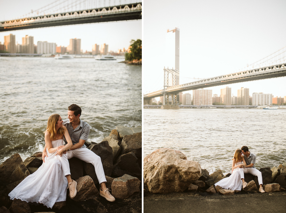 Man and woman sit on large rocks next to the East River with the Brooklyn Bridge behind them