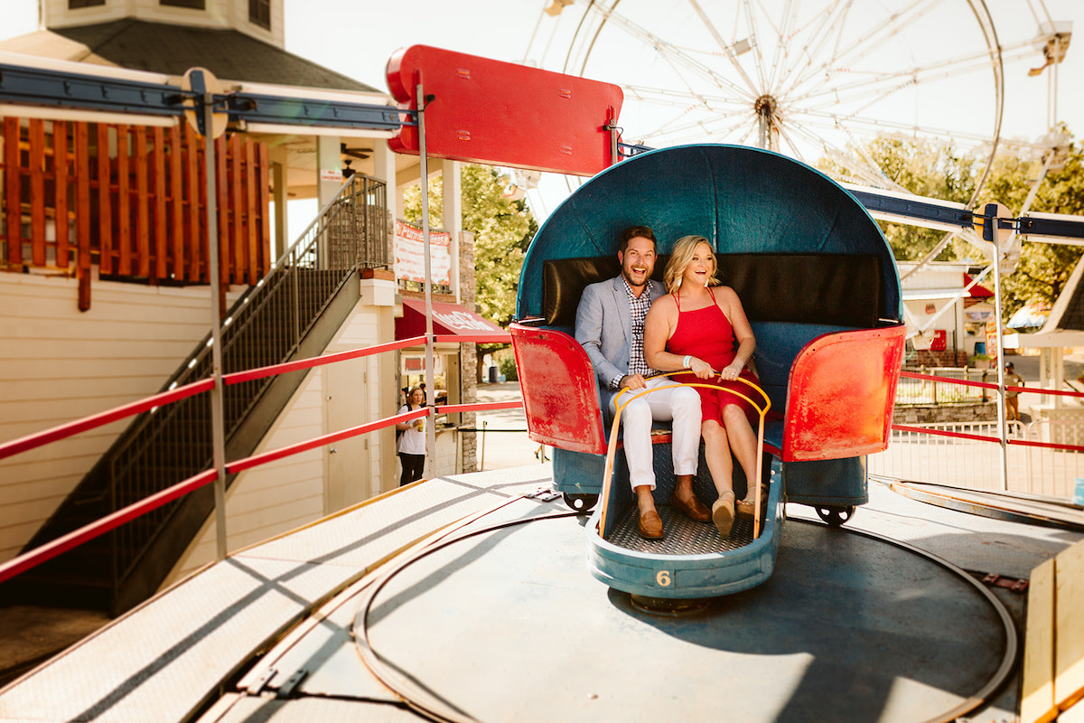 Man and woman laugh in blue and red spinning carnival ride during their engagement photos at Lake Winnie in Chattanooga, TN