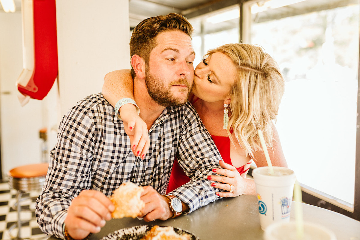 Woman kisses man's cheek as he enjoys a funnel cake