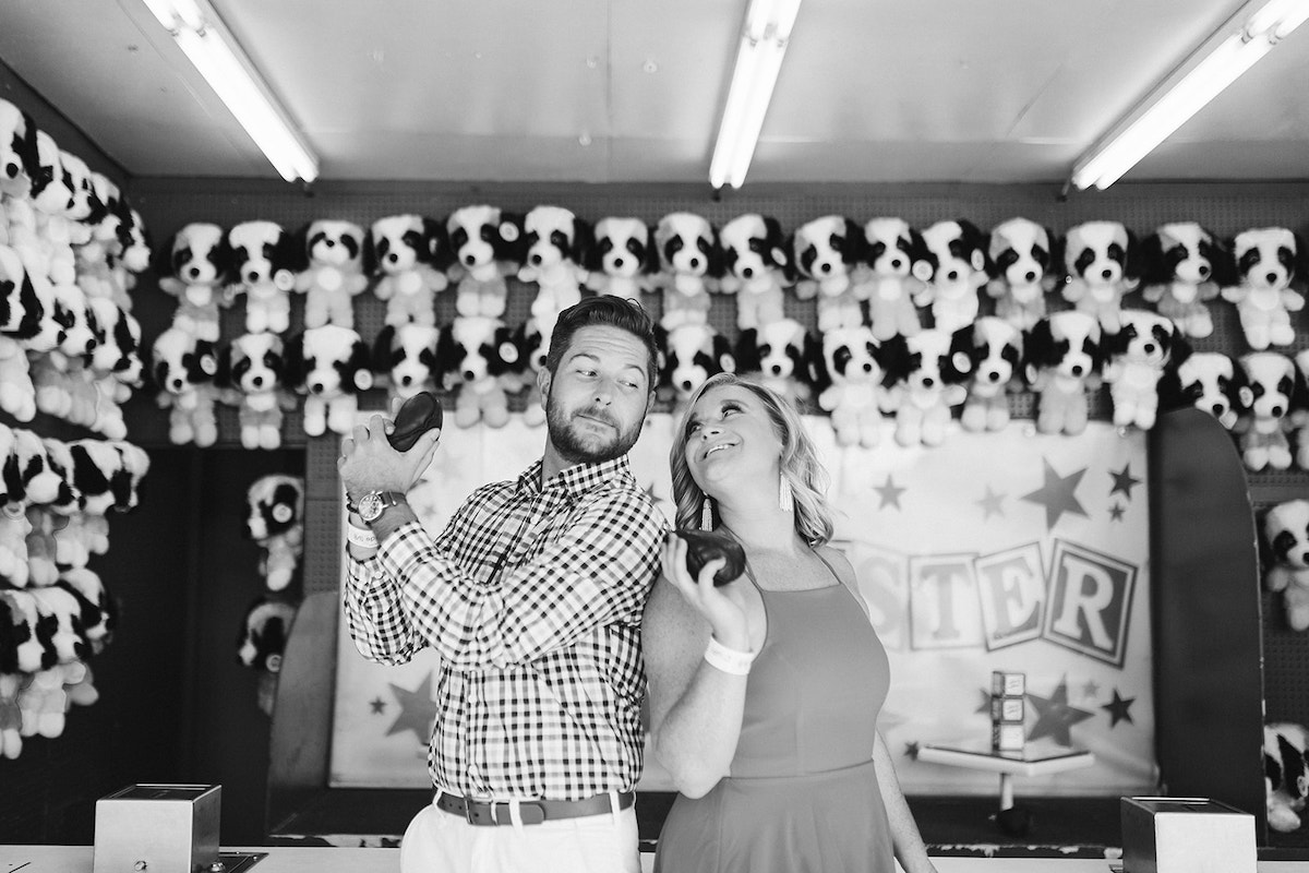 Man and woman hold bean bags in front of carnival game counter as they prepare to toss bags for stuffed animal prize