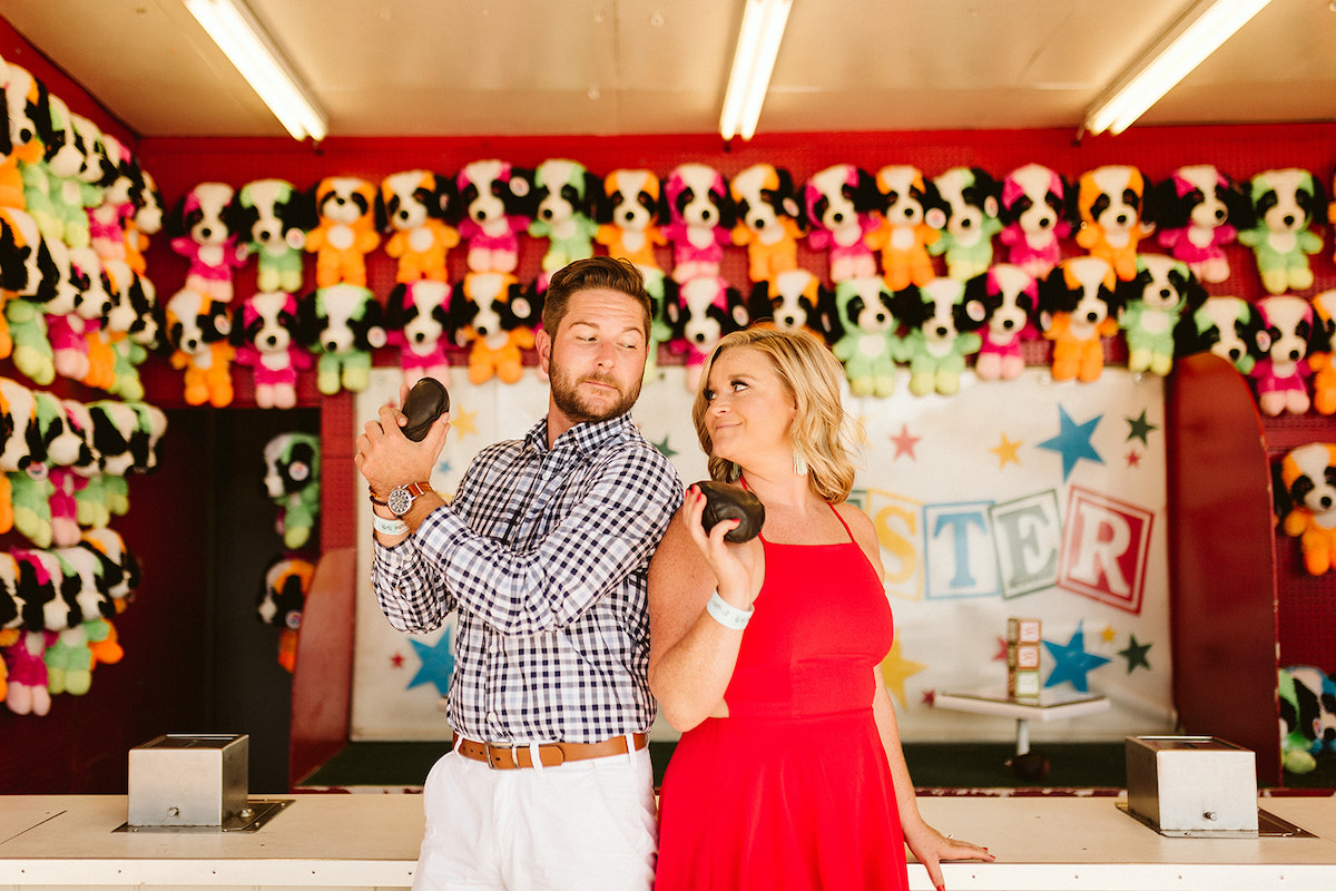 Man and woman hold bean bags in front of carnival game counter as they prepare to toss bags for stuffed animal prize