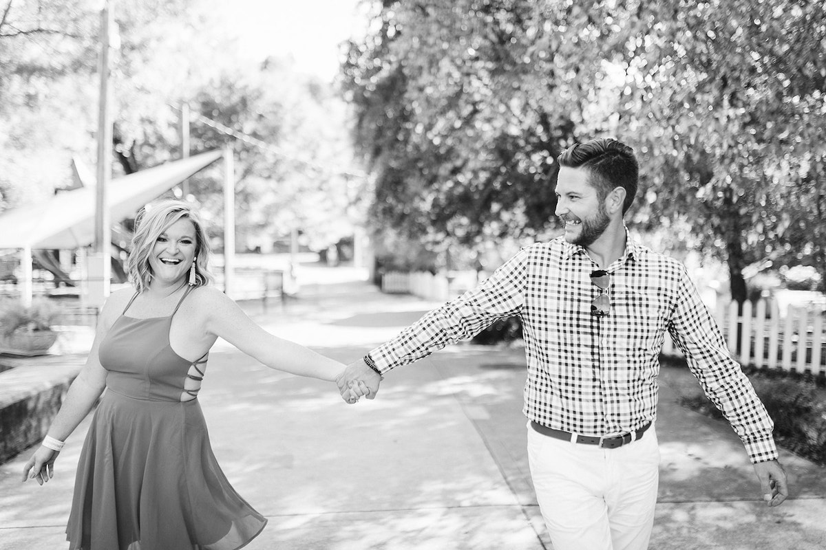 Man and woman hold hands and smile while walking on sidewalk