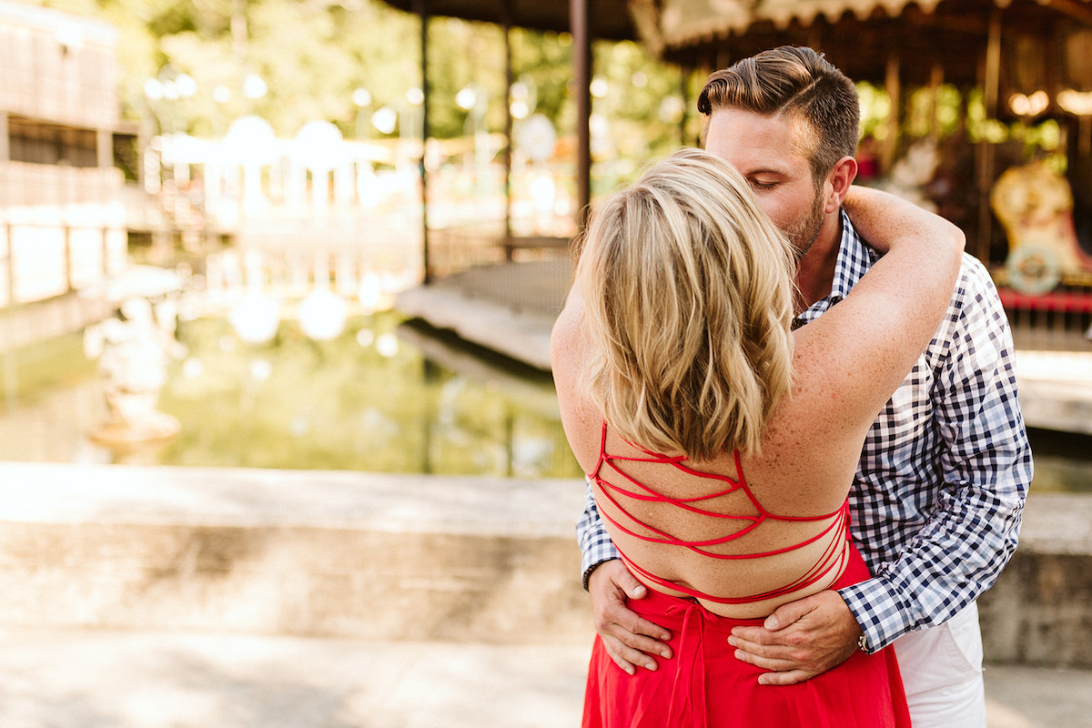 Woman in red backless dress kisses her fiance