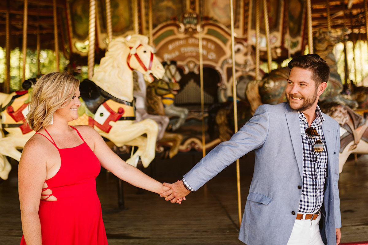 Man holds woman's hand and leads her past carousel