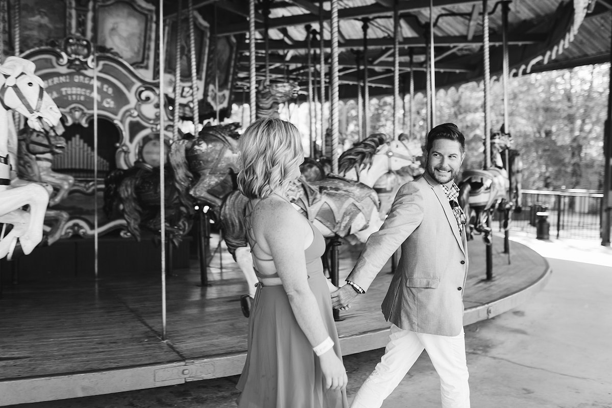 Man holds woman's hand and leads her past carousel