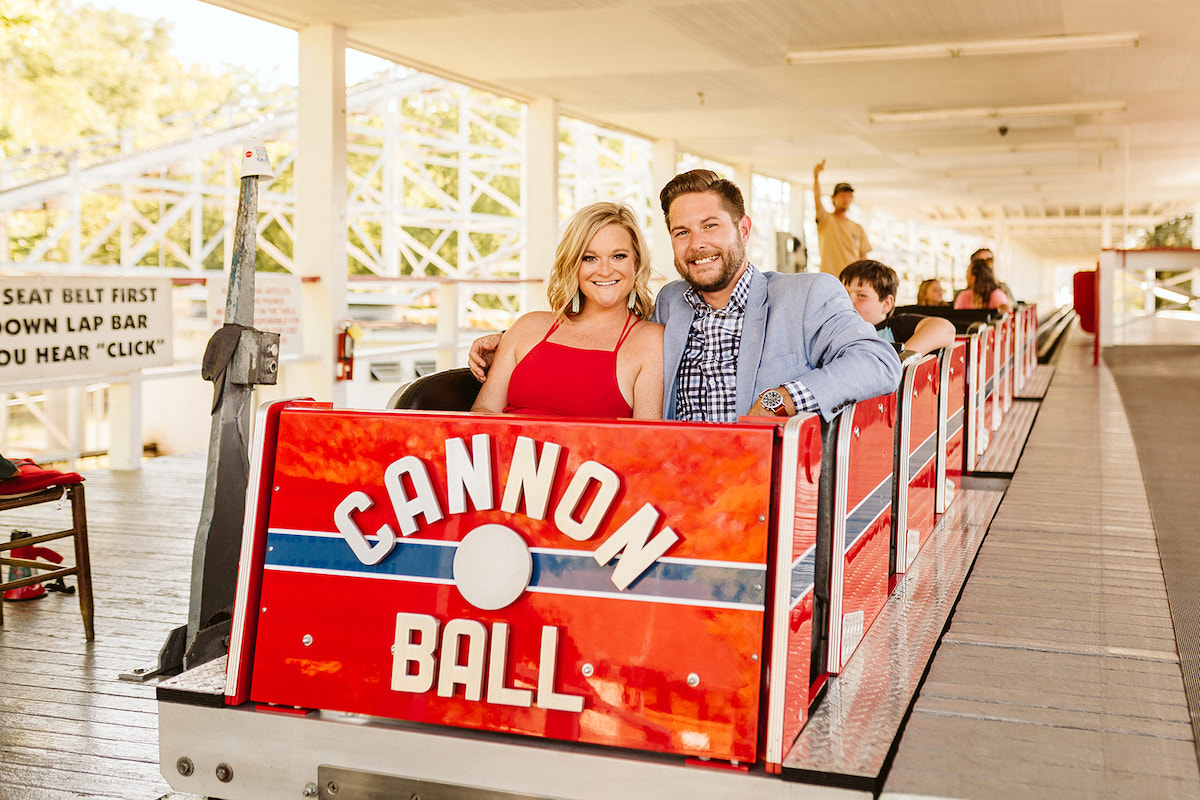 Man and woman sit in the first car of the Cannon Ball rollercoaster during their fun engagement photos at Lake Winnie
