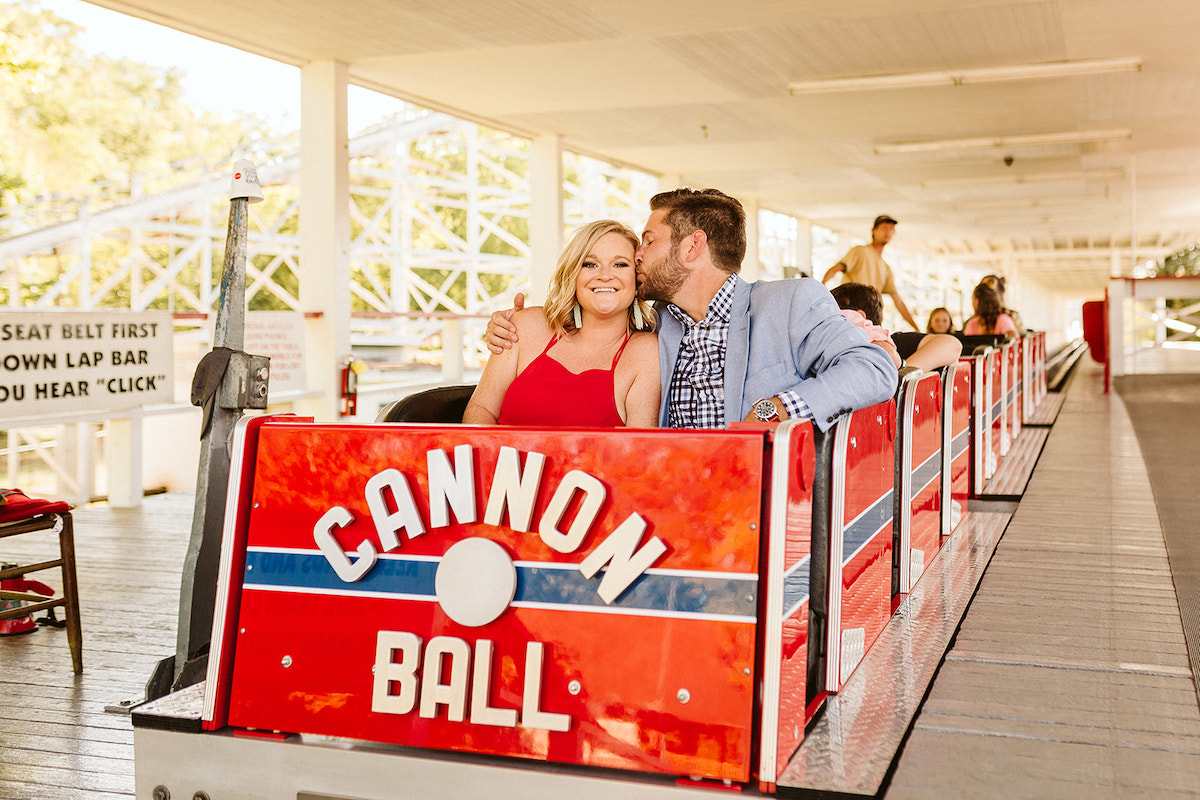 Man kisses woman's cheek in the first car of the Cannon Ball rollercoaster during their fun engagement photos at Lake Winnie