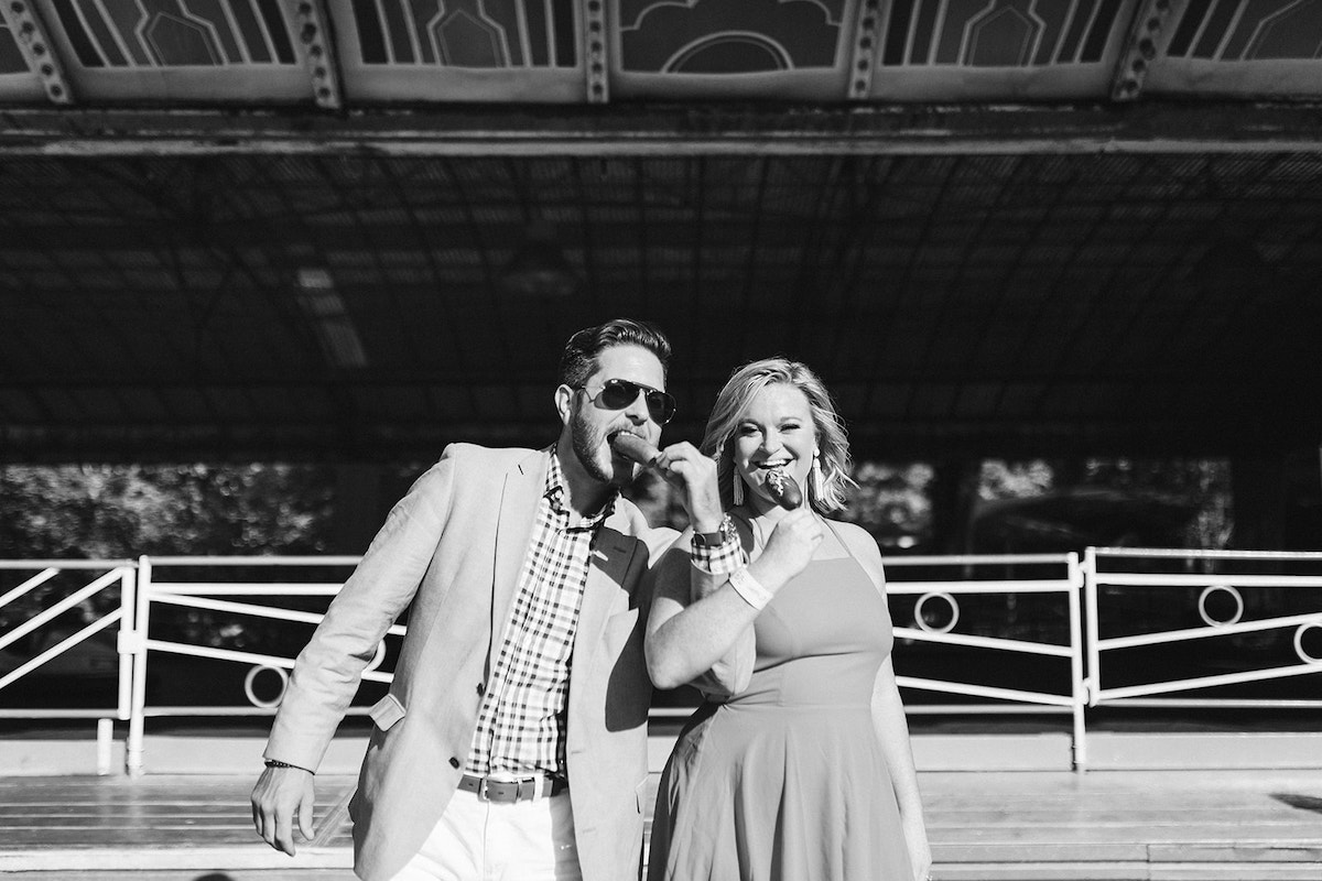 Man and woman link arms and bite into fried corn dogs during their fun engagement photo session in Chattanooga, TN