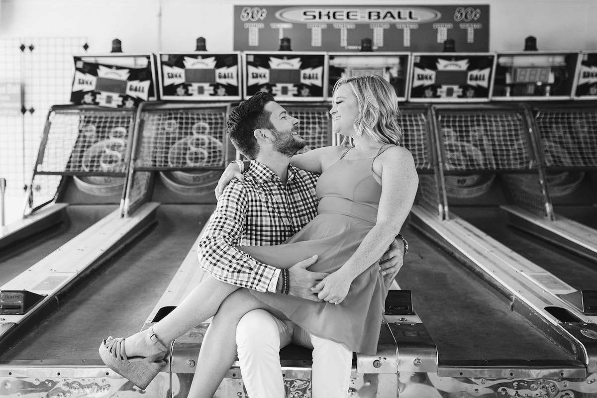 Woman sits on man's lap on the Skee-ball arcade game for their fun engagement photos at Lake Winnie in Chattanooga, TN