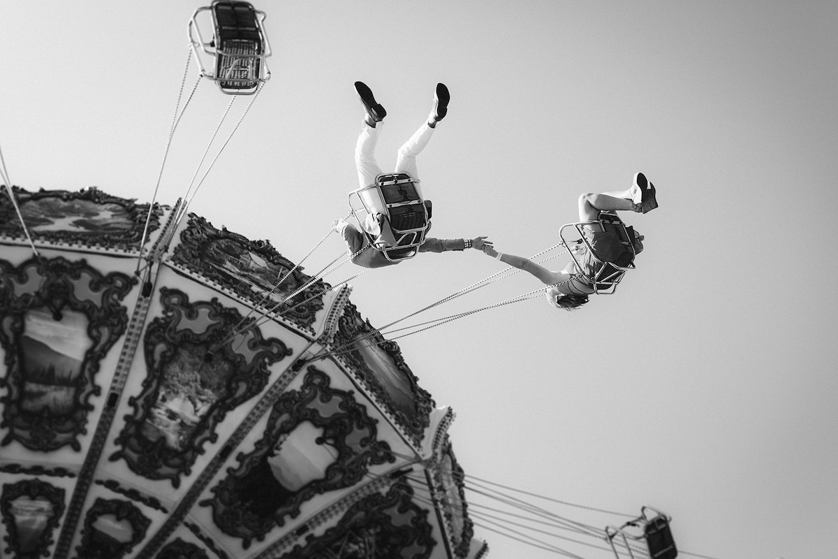 Man and woman reach for each other's hands on the swing carousel ride for their fun engagement photos at Lake Winnie