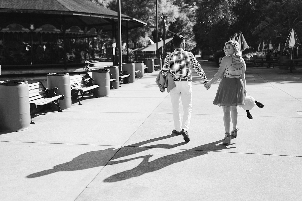 Man and woman holding hands and walking. She carries a stuffed puppy carnival game prize.