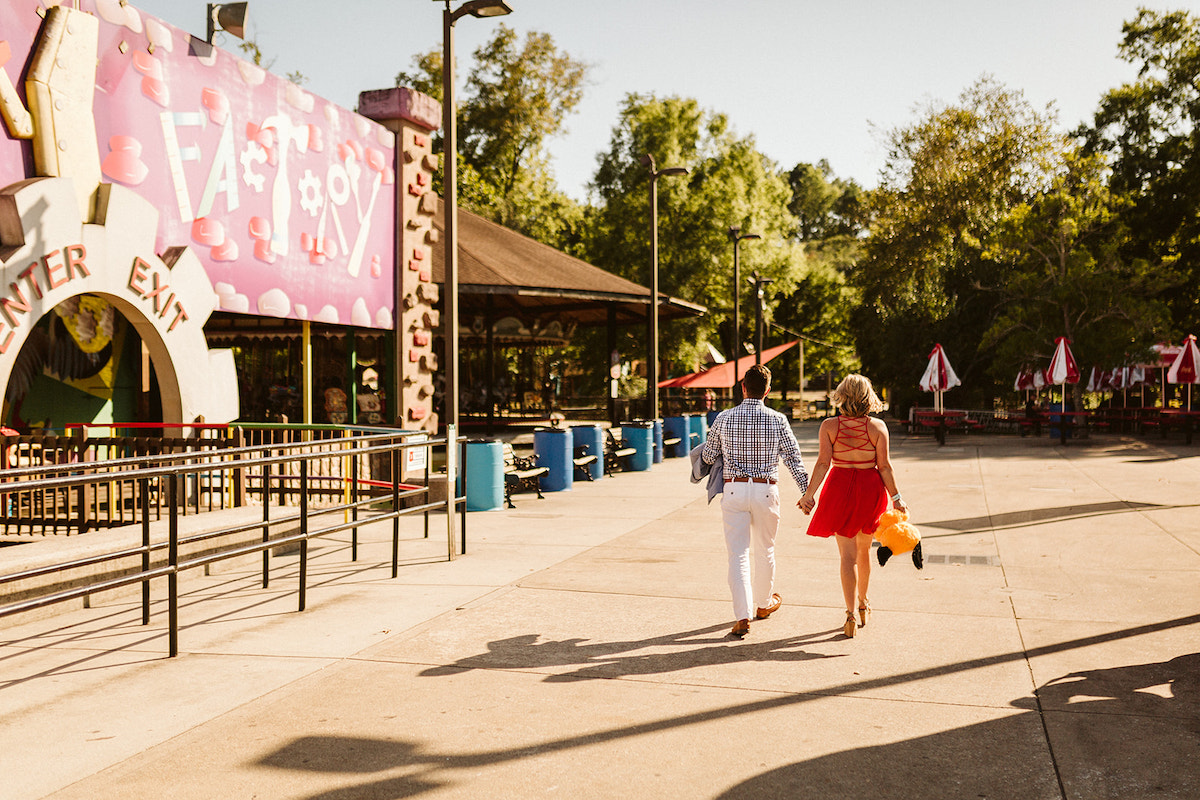 Man and woman holding hands and walking. She carries a stuffed puppy carnival game prize.