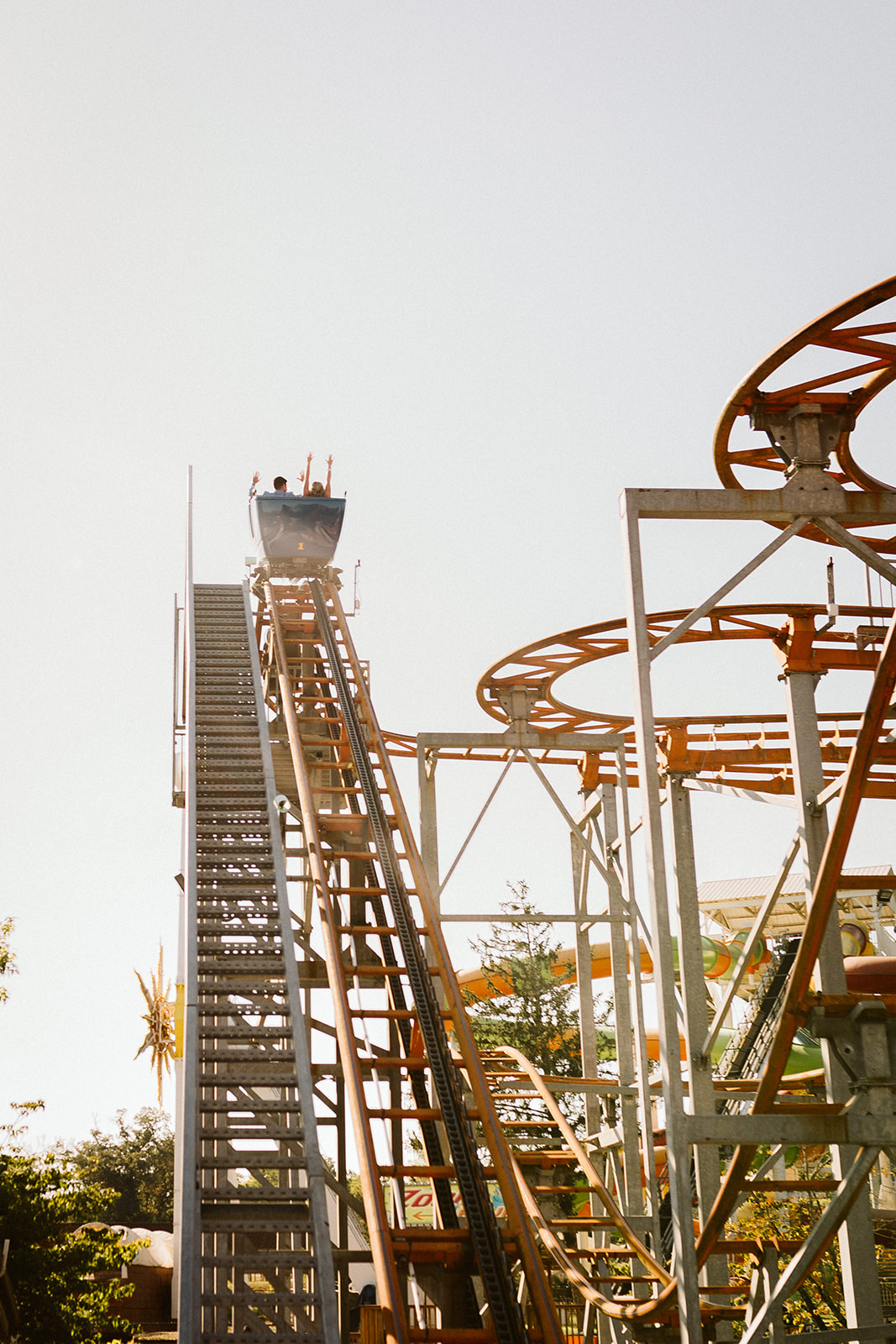 Roller coaster car at the top of a steep climb. People raise their hands at the top.