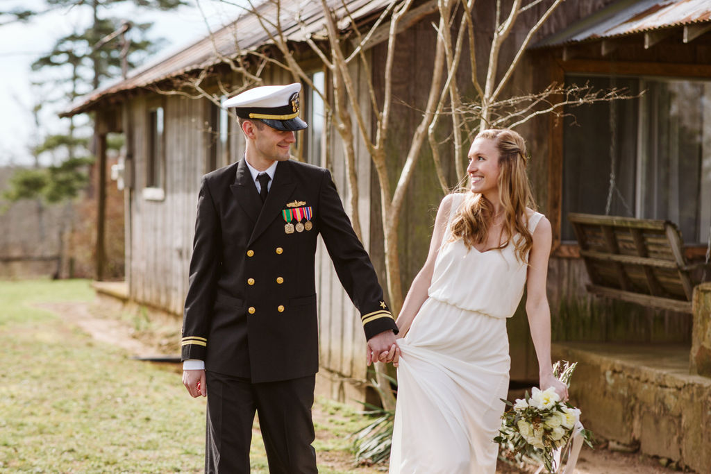 Groom in military dress uniform holds his bride's hand as they smile at each other