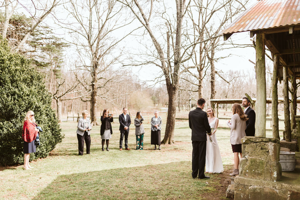 Bride and groom face each other holding hands in front of antique cabin porch during their elopement ceremony
