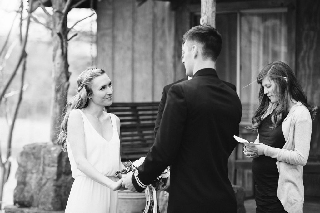 Bride and groom face each other holding hands in front of antique family cabin porch at their intimate elopement wedding