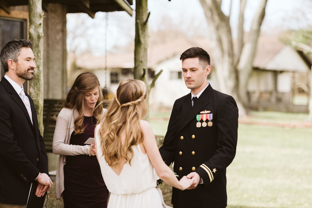 Bride and groom facing each other holding hands in front of antique family cabin porch